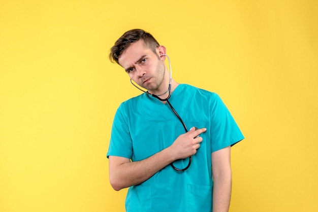 Vorderansicht des jungen männlichen Arztes mit Stethoskop auf gelber Wand