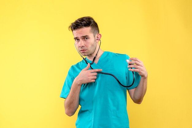 Vorderansicht des jungen männlichen Arztes mit Stethoskop auf hellgelber Wand
