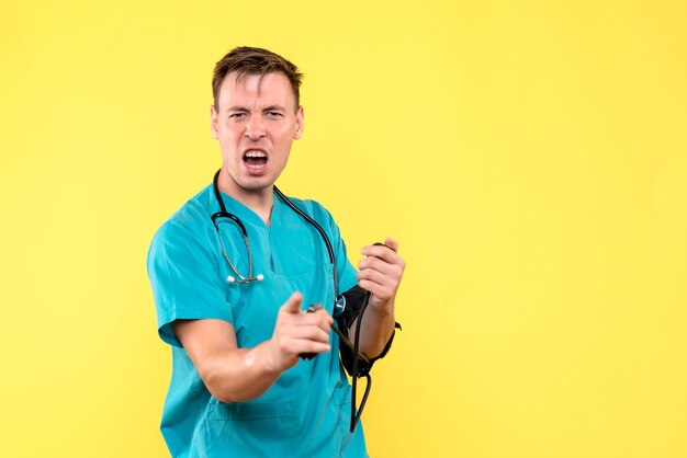 Vorderansicht des jungen männlichen Arztes unter Verwendung des Tonometers auf gelber Wand