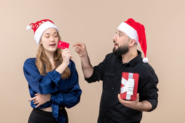 Vorderansicht des jungen Mannes, der Geschenk mit Frau hält, die Bankkarte auf rosa Wand hält