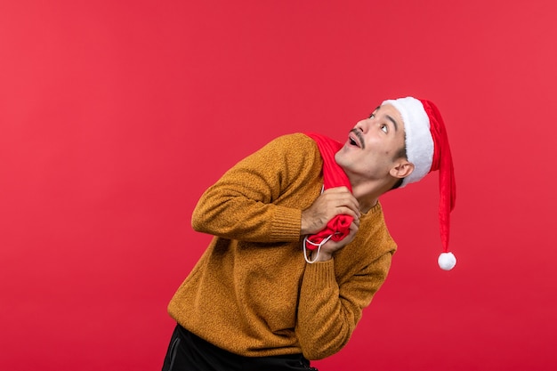 Vorderansicht des jungen Mannes, der Geschenkbeutel auf der roten Wand trägt