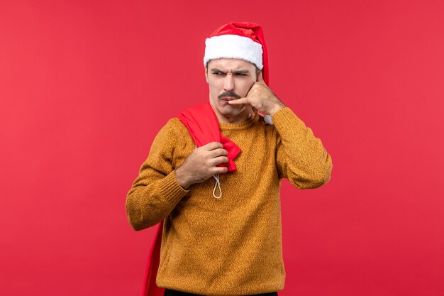 Vorderansicht des jungen Mannes, der Geschenkbeutel auf der roten Wand trägt