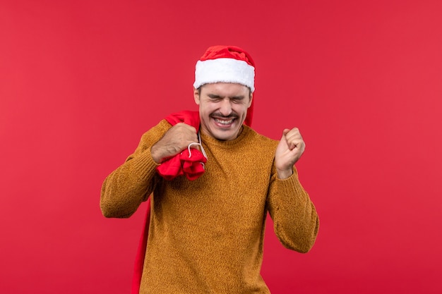 Vorderansicht des jungen Mannes, der Geschenkbeutel auf hellroter Wand trägt