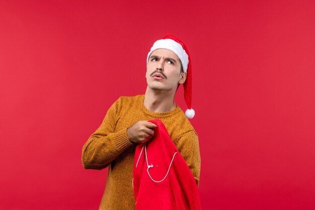 Vorderansicht des jungen Mannes, der Geschenke von der Tasche an der roten Wand herausnimmt