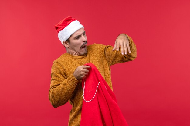 Vorderansicht des jungen Mannes, der Geschenke von der Tasche an der roten Wand herausnimmt