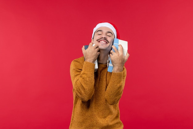 Vorderansicht des jungen Mannes, der Geschenkkästen an der roten Wand hält