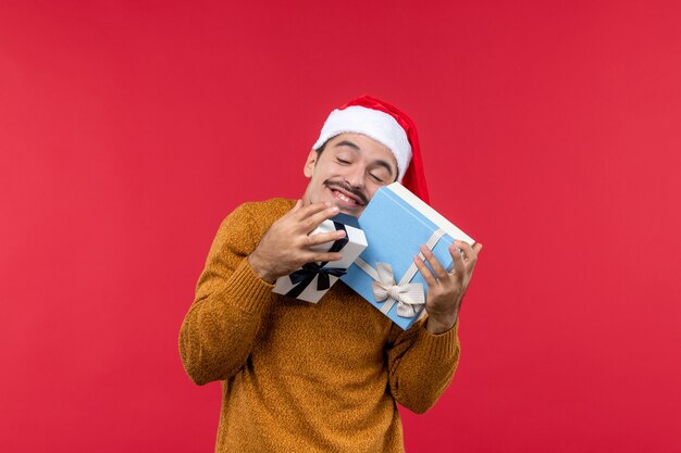 Vorderansicht des jungen Mannes, der Geschenkkästen an der roten Wand hält