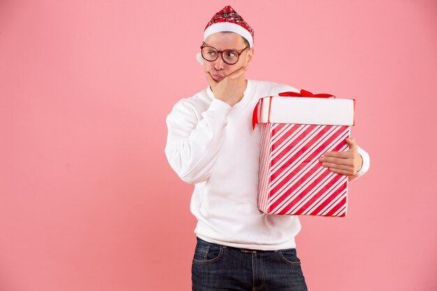 Kostenloses Foto vorderansicht des jungen mannes, der großes geschenk an der rosa wand hält