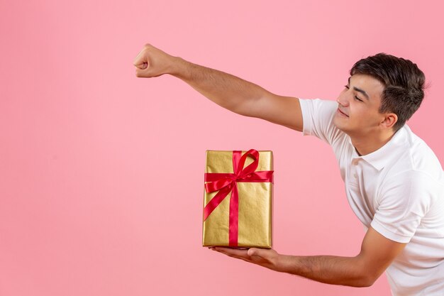 Vorderansicht des jungen Mannes, der jemandem an der rosa Wand Weihnachtsgeschenk gibt