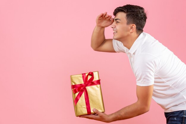 Vorderansicht des jungen Mannes, der jemandem an der rosa Wand Weihnachtsgeschenk gibt