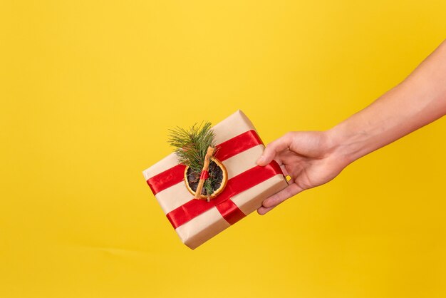 Vorderansicht des jungen Mannes, der kleines Weihnachtsgeschenk auf gelber Wand hält