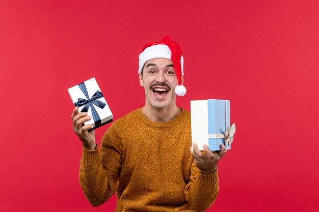 Vorderansicht des jungen Mannes, der Neujahrsgeschenke an der roten Wand hält