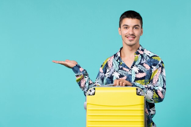 Vorderansicht des jungen Mannes, der Reise mit seiner gelben Tasche vorbereitet, die auf blaue Wand lächelt