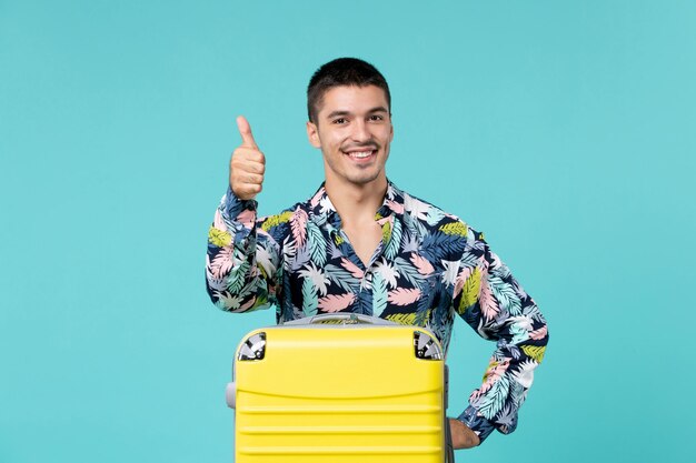 Vorderansicht des jungen Mannes, der Reise mit seiner gelben Tasche vorbereitet, die auf blaue Wand lächelt