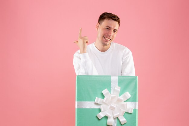 Vorderansicht des jungen Mannes, der sich im Geschenk der rosa Wand versteckt