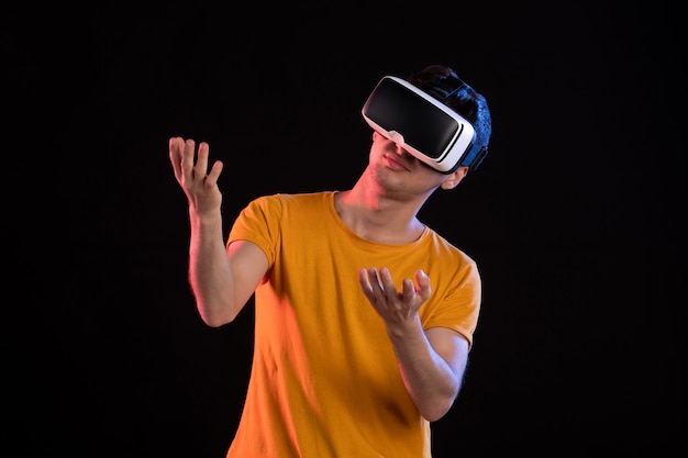 Vorderansicht des jungen Mannes, der virtuelle Realität an der dunklen Wand spielt