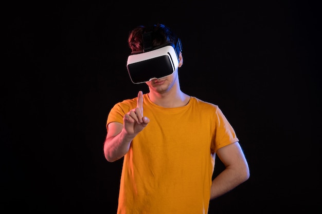 Vorderansicht des jungen Mannes, der virtuelle Realität an der dunklen Wand spielt