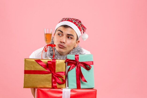 Vorderansicht des jungen Mannes, der Weihnachten um Geschenke auf rosa Wand feiert