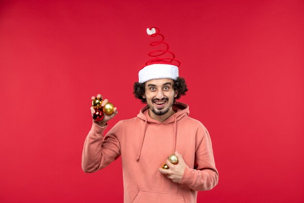 Kostenloses Foto vorderansicht des jungen mannes, der weihnachtsbaumspielzeug an der roten wand hält