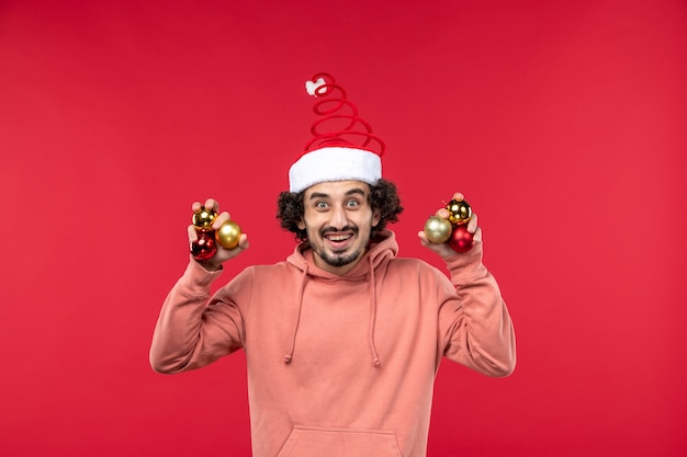 Kostenloses Foto vorderansicht des jungen mannes, der weihnachtsbaumspielzeug an der roten wand hält