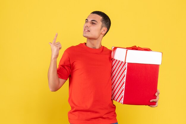 Vorderansicht des jungen Mannes, der Weihnachtsgeschenk auf gelber Wand hält