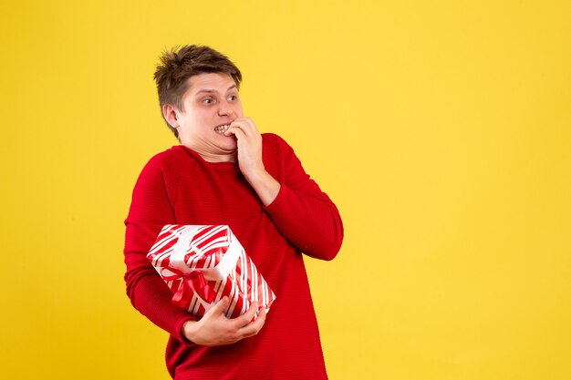 Vorderansicht des jungen Mannes, der Weihnachtsgeschenk auf gelber Wand hält