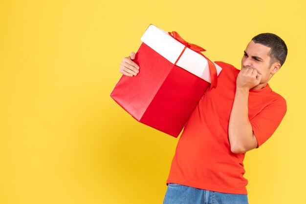 Vorderansicht des jungen Mannes, der Weihnachtsgeschenk auf gelber Wand hält