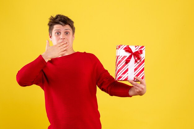 Vorderansicht des jungen Mannes, der Weihnachtsgeschenk auf gelber Wand hält