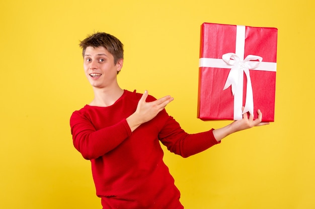 Vorderansicht des jungen Mannes, der Weihnachtsgeschenk auf gelber Wand hält