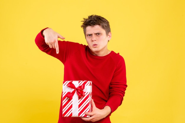Vorderansicht des jungen Mannes, der Weihnachtsgeschenk auf gelber Wand hält