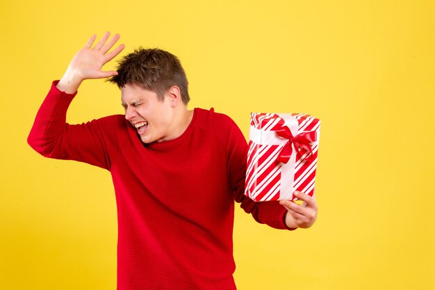 Vorderansicht des jungen Mannes, der Weihnachtsgeschenk auf gelber Wand hält