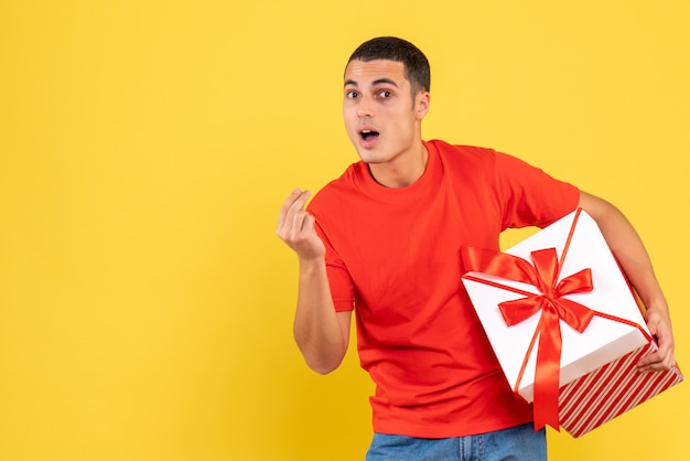 Vorderansicht des jungen Mannes, der Weihnachtsgeschenk auf gelber Wand hält