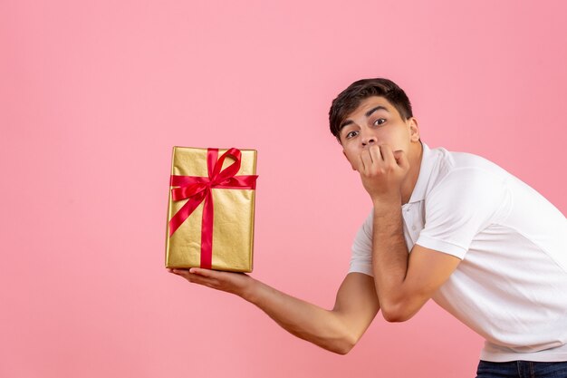 Vorderansicht des jungen Mannes, der Weihnachtsgeschenk auf rosa Wand hält