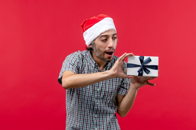 Vorderansicht des jungen Mannes, der Weihnachtsgeschenk auf Rot hält