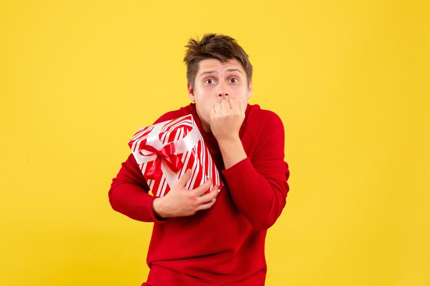 Vorderansicht des jungen Mannes, der Weihnachtsgeschenk hält, erschreckte auf gelber Wand