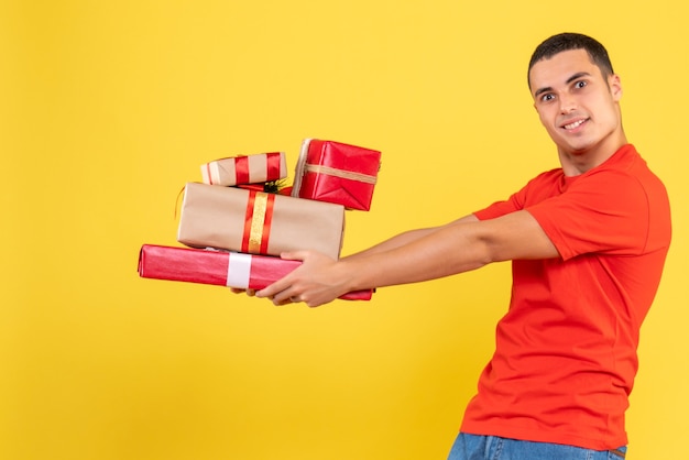 Vorderansicht des jungen Mannes, der Weihnachtsgeschenke auf gelber Wand hält