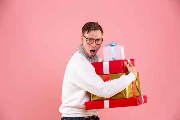 Vorderansicht des jungen Mannes, der Weihnachtsgeschenke auf rosa Wand hält