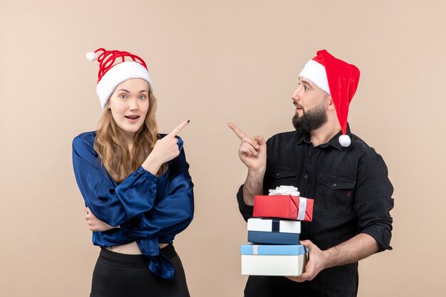 Vorderansicht des jungen Mannes, der Weihnachtsgeschenke mit Frau an der rosa Wand hält