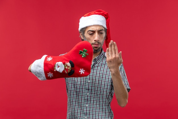 Vorderansicht des jungen Mannes, der Weihnachtssocke auf roter Wand trägt