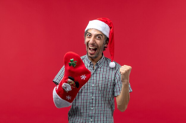 Vorderansicht des jungen Mannes, der Weihnachtssocke auf roter Wand trägt