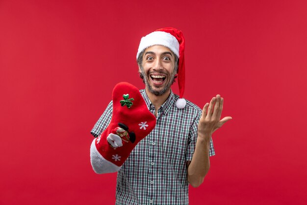 Vorderansicht des jungen Mannes, der Weihnachtssocke auf roter Wand trägt