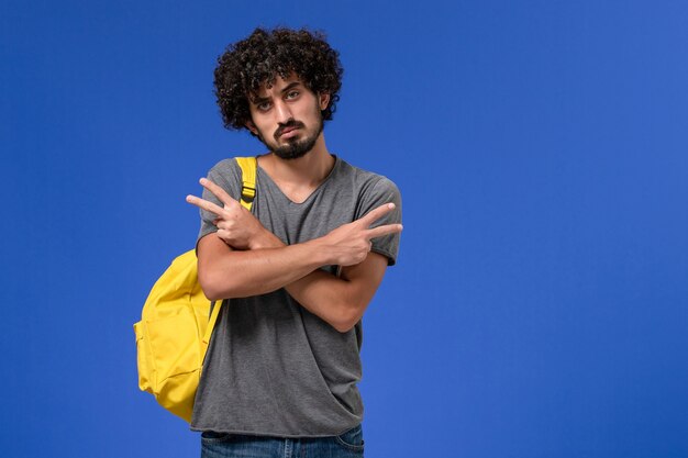 Vorderansicht des jungen Mannes im grauen T-Shirt, das gelben Rucksack trägt, der gerade auf der blauen Wand aufwirft