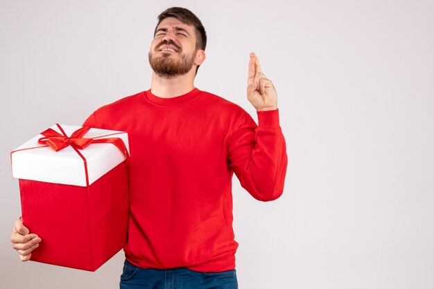 Vorderansicht des jungen Mannes im roten Hemd, das Weihnachtsgeschenk im Kasten auf weißer Wand hält