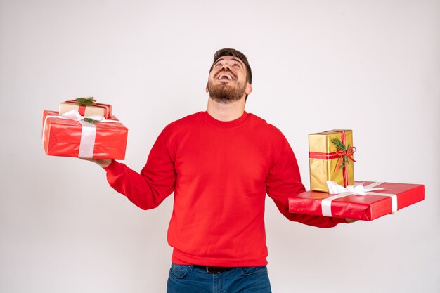 Vorderansicht des jungen Mannes im roten Hemd, das Weihnachtsgeschenke auf weißer Wand hält