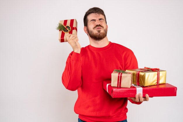 Vorderansicht des jungen Mannes im roten Hemd, das Weihnachtsgeschenke auf weißer Wand hält