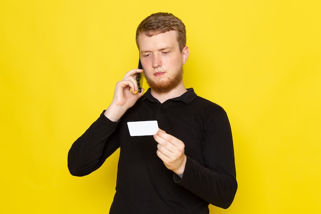 Vorderansicht des jungen Mannes im schwarzen Hemd, das am Telefon spricht, das weiße Karte hält