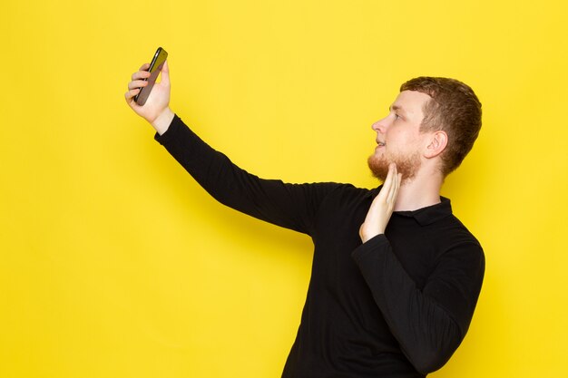 Vorderansicht des jungen Mannes im schwarzen Hemd, das ein selfie nimmt