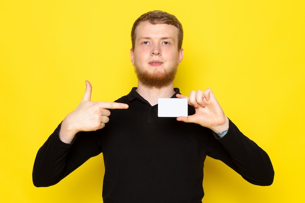 Kostenloses Foto vorderansicht des jungen mannes im schwarzen hemd, das weiße karte auf der gelben oberfläche hält