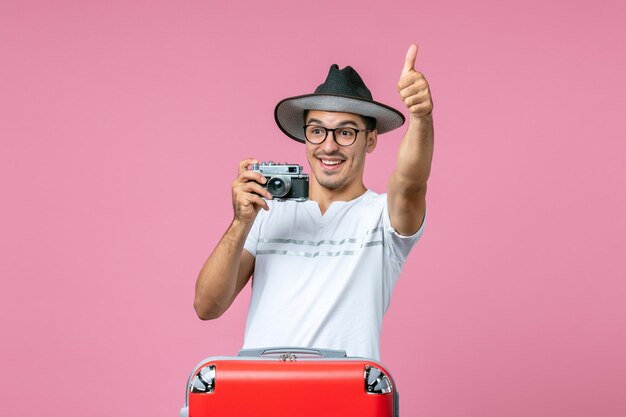 Vorderansicht des jungen Mannes im Urlaub mit Tasche mit Kamera, die Fotos an der rosa Wand macht