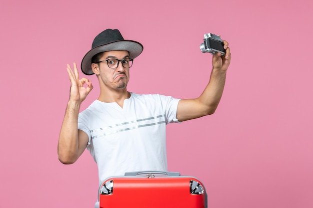 Kostenloses Foto vorderansicht des jungen mannes im urlaub mit tasche mit kamera, die fotos an hellrosa wand macht